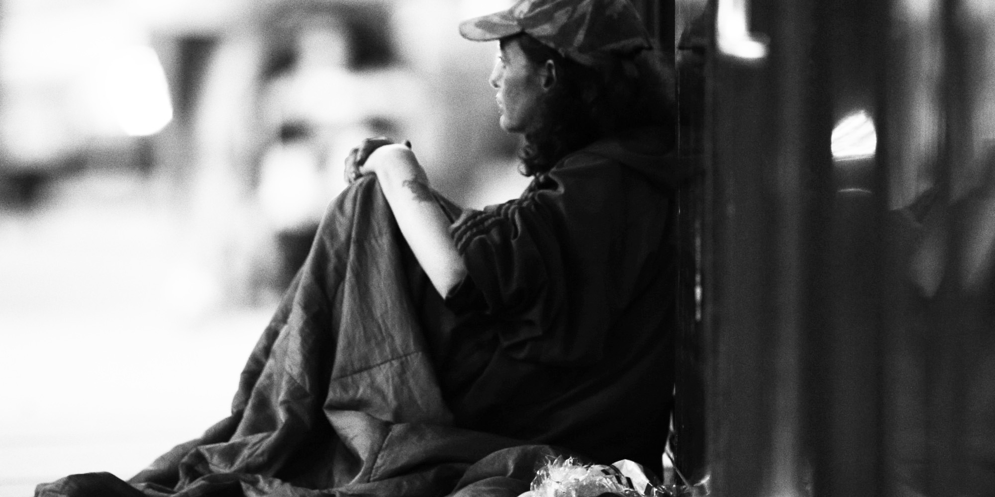 A woman who is homeless sitting on the sidewalk.