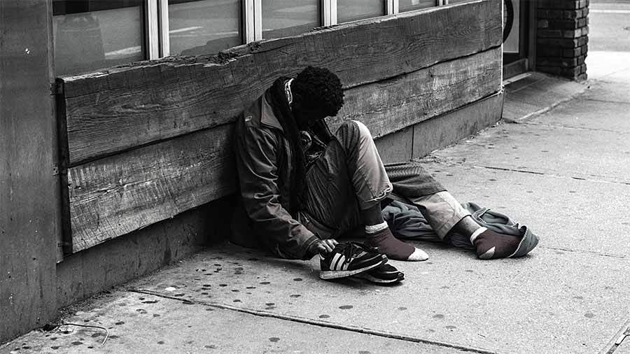 A black man sits on the sidewalk against the side of a building. A human in need of Christ's love and restoration.
