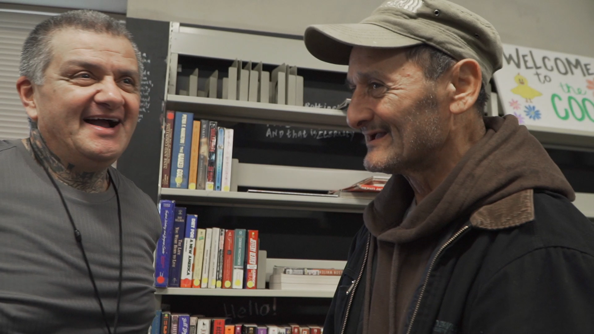 A staff member and a guest of Lighthouse Mission (both male) stand near each other and are laughing.