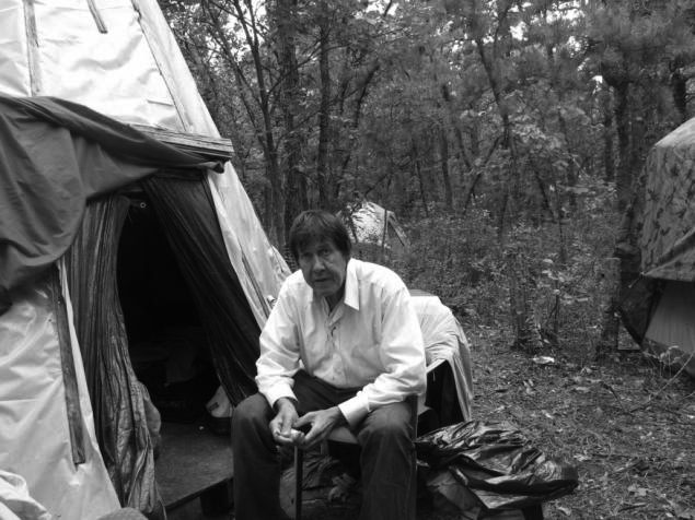 A man sitting outdoors near the entrance of a tent.