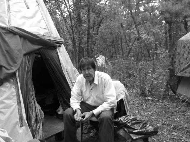 A man sitting outdoors near the entrance of a tent. And Lighthouse will make a difference in his life through your giving.